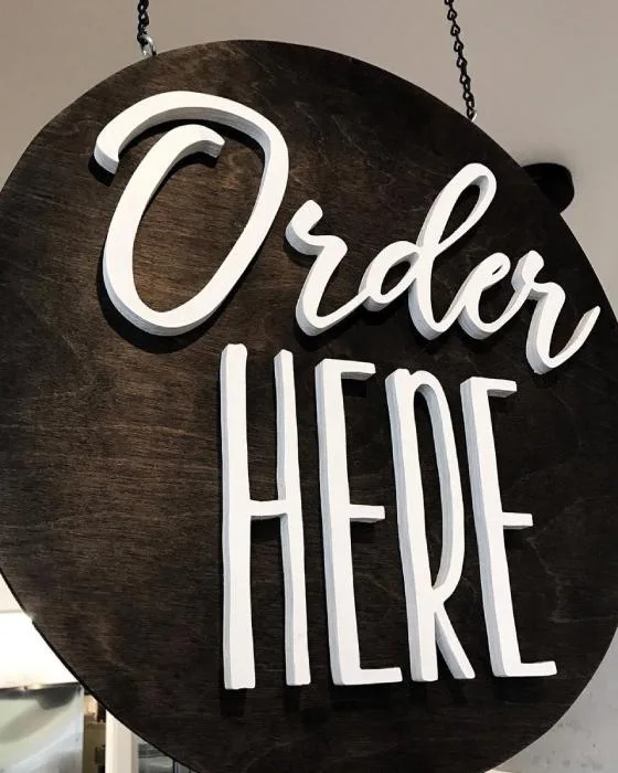 Cartel redondo de madera con letras corpóreas blancas "Order Here" de Gavalmedia